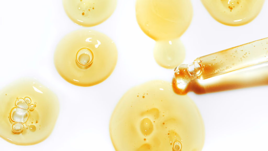 Makroaufnahme einer Pipette, aus der transparente Tropfen eines Serums auf eine glatte Oberfläche fallen.