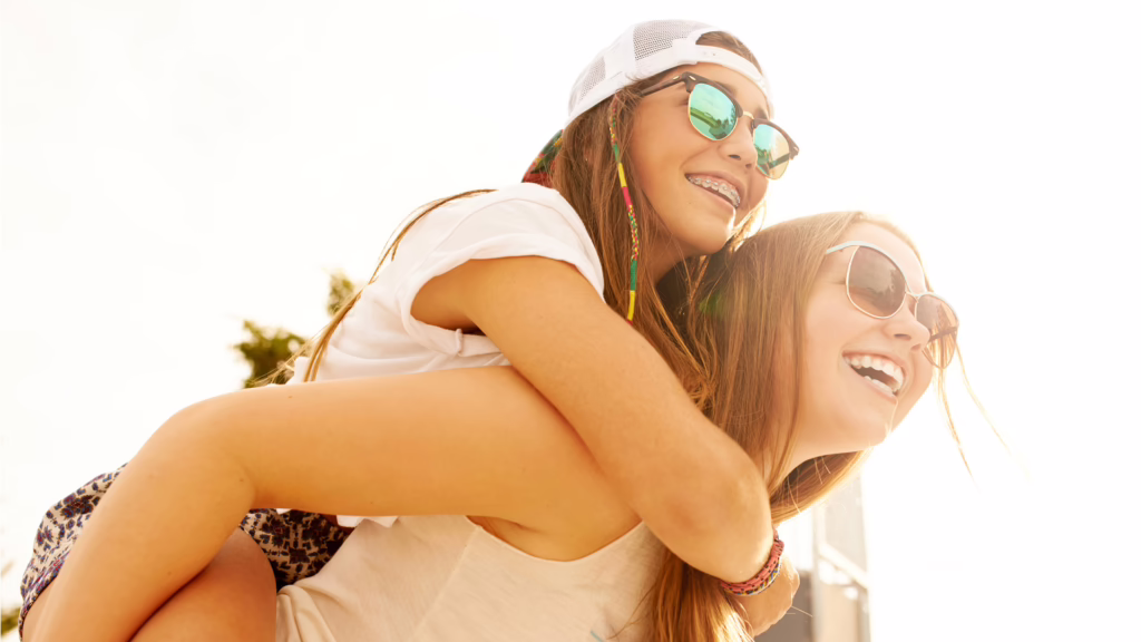 Eine junge Frau trägt eine andere Frau lachend Huckepack.