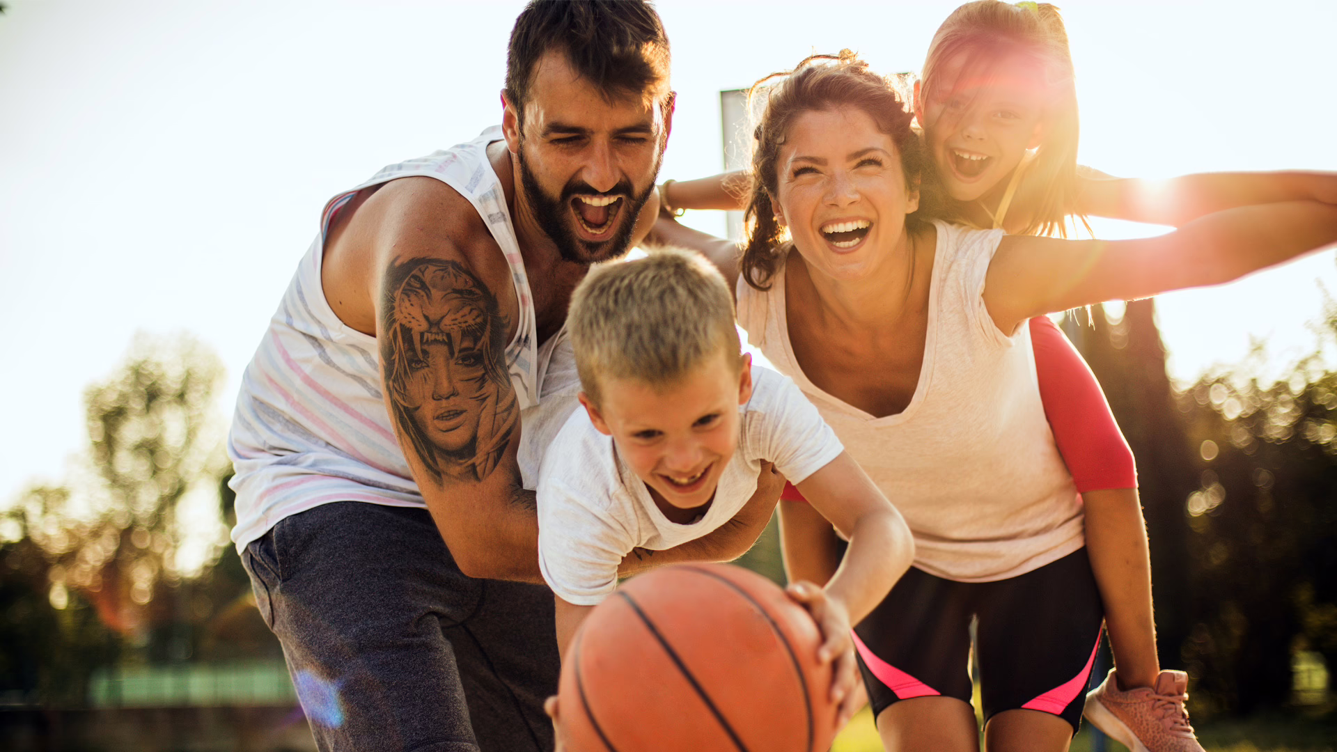 Glückliche Familie beim Basketballspielen in der Sonne.
