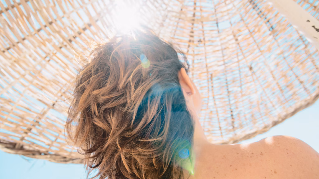 Eine Frau mit mittellangem Haar unter einem Stroh-Sonnenschirm von hinten zu sehen.